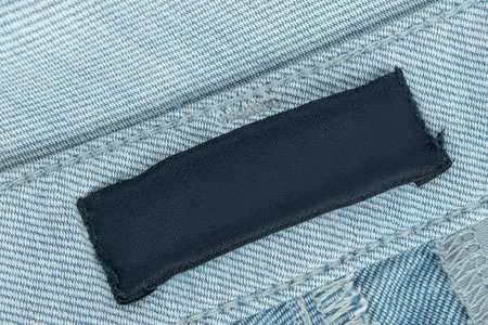 Blank clothes patch label stitched on light blue cotton fabric background closeupの写真素材