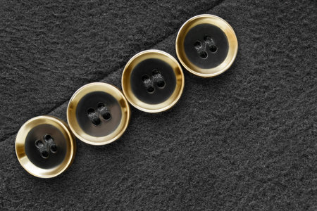 Four small gilded coat buttons sewn on black wool fabric background