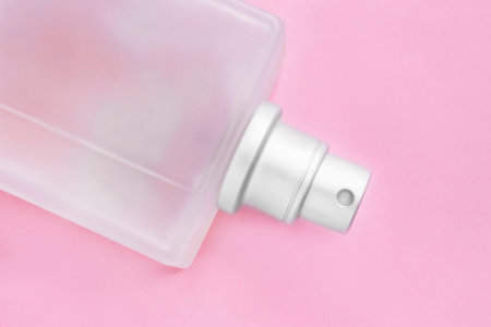 Frosted glass perfume spray bottle lying on pink background