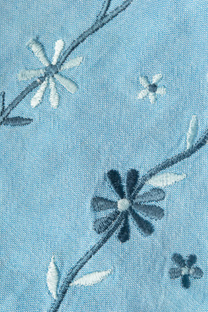Floral silk embroidery on light blue cotton fabric closeup as a backgroundの写真素材