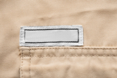 Blank clothes patch label stitched on beige fabric backgroundの写真素材