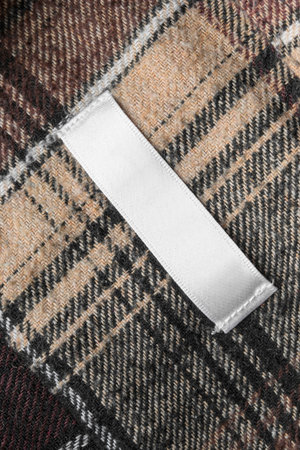 Blank clothes label stitched on brown tartan wool fabric as a backgroundの写真素材