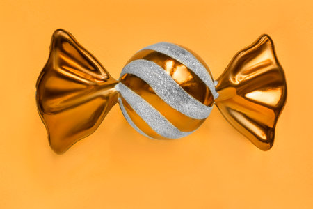 Golden glass candy shaped christmas toy over yellow studio backgroundの写真素材