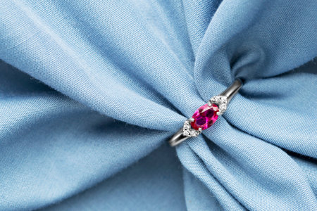 Silver ring with pink gemstone and diamonds on pastel blue draped fabricの写真素材