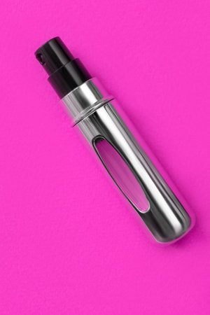 Perfume spray atomizer lying over fuchsia pink studio background