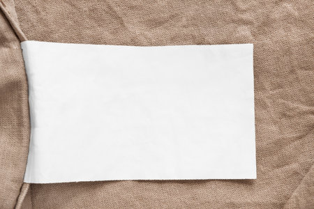 Blank white clothes label over beige linen fabric background closeupの写真素材