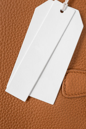 Blank white price tag label over brown leather background closeupの写真素材