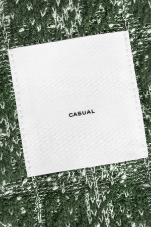 Clothes label text Casual stitched on dark green knit background closeup