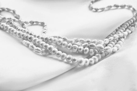 White natural pearl necklace lying on white silk fabric backgroundの写真素材