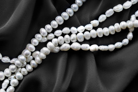 White natural pearl necklace lying over black draped silk fabric