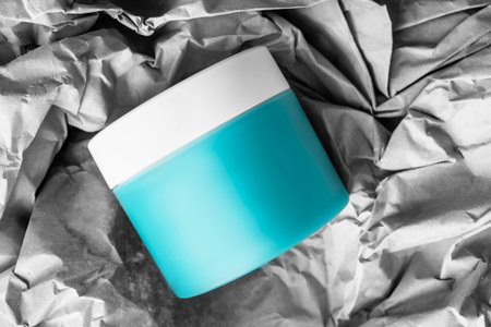 Beauty product plastic jar lying over crumpled wrapping craft paper backgroundの写真素材