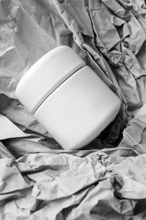 Blank white beauty product jar lying on crumpled packaging paper background