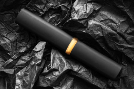Black matte lipstick tube lying over black crumpled wrapping paper backgroundの写真素材