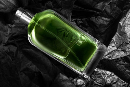 Green perfume glass bottle over black crumpled wrapping paper background