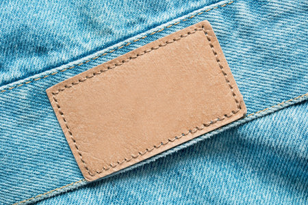 Empty patch label stitched on light blue denim fabric background closeup