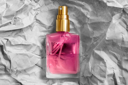 Pink glass perfume spraying bottle over white crumpled craft paper backgroundの写真素材