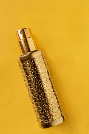 Golden perfume atomizer over yellow color studio background