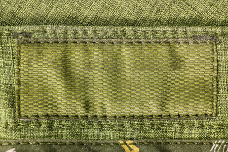 Blank clothes label patch closeup stitched on khaki green fabric background