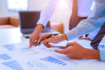 Young businessman holding pen pointing to graph and chart in the office. Accounting and finance...