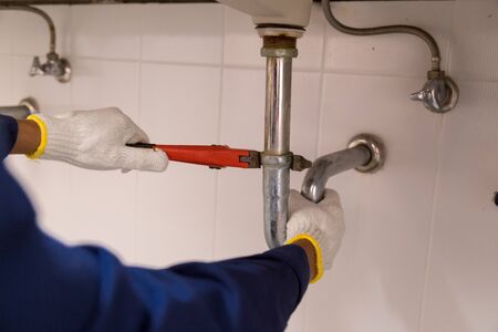 Plumber fixing white sink pipe with adjustable wrench.の写真素材