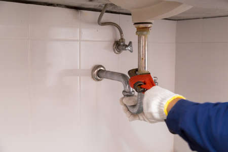 Plumber fixing white sink pipe with adjustable wrench.の写真素材