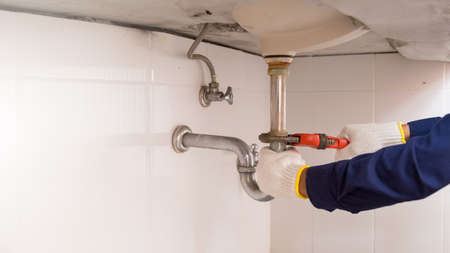 Plumber fixing white sink pipe with adjustable wrench.の写真素材