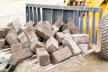 Pile of bricks on sieve scoop of small excavator