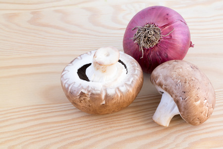 Two chestnut mushrooms and a red onion on a wooden cutting boardの写真素材