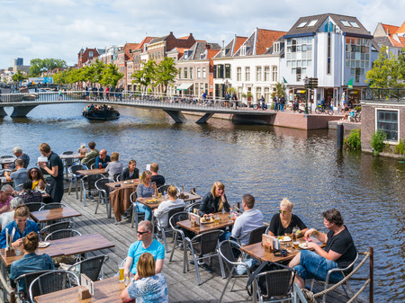 People on outdoor terrace of cafe, bridge and historic gables on quay of Rhine canal in old town of Leiden, South Holland, Netherlandsのeditorial素材