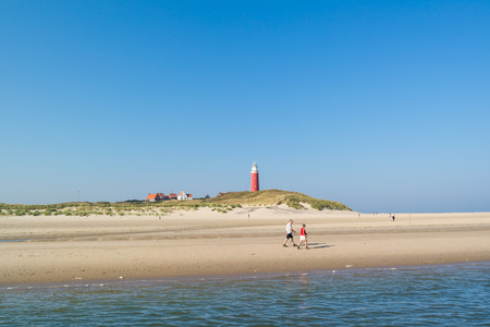 TEXEL, NETHERLANDS - SEP 14, 2016: Active pensioners walking on beach and De Cocksdorp lighthouse on West Frisian Waddensea island Texel, Netherlandsのeditorial素材
