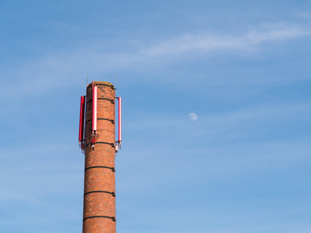 Old stack with mobile telephony transmitter against blue sky and moon, Netherlandsの写真素材