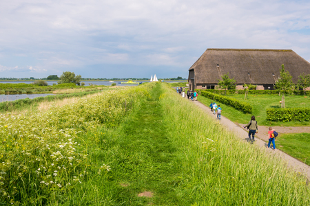 TIENGEMETEN, NETHERLANDS - MAY 20, 2017: Dike with grass and flowers, farmhouse and people walking on footpath on Tiengemeten island in Haringvliet estuary, South Holland, Netherlandsのeditorial素材