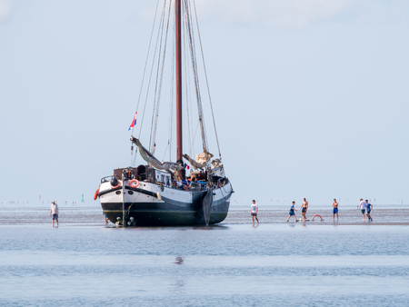Group of youngsters playing on sand flat and dried out flat-bottom sailing yacht at low tide on Wadden sea, Netherlandsのeditorial素材