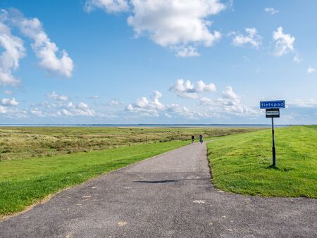 People riding bicycles on bicycle path between dike and salt marshes on West Frisian island Schiermonnikoog, Netherlandsのeditorial素材