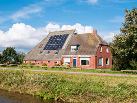 Farmhouse with 18 solar panels on roof by Dokkumer Ee canal in Friesland, Netherlandsの写真素材