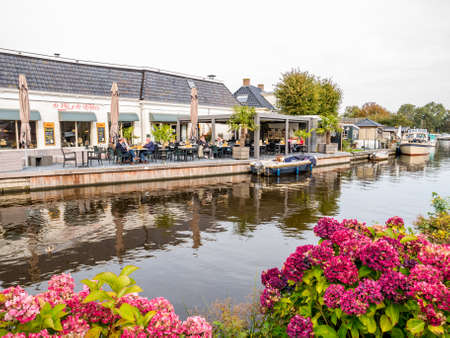 People on outdoor terrace of cafe restaurant by canal in old village of Wartena, Leeuwarden, Netherlandsのeditorial素材