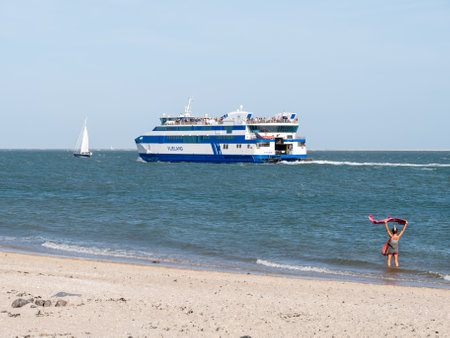 Woman waving goodbye to passengers on ferry boat leaving harbor of West Frisian island Vlieland crossing Waddensea to Harlingen, Netherlandsのeditorial素材