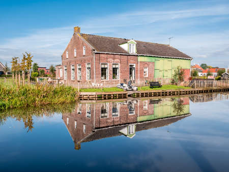 WARGA, NETHERLANDS - SEP 19, 2017: House and barn reflecting in water of Wargaastervaart in village of Wergea, Leeuwarden, Frieslandのeditorial素材