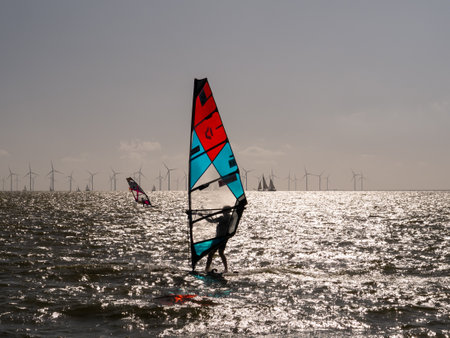Windsurfer with red and blue sail backlit on IJsselmeer lake near Makkum, Friesland, Netherlandsのeditorial素材