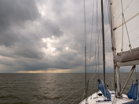Sailboat sailing downstream on Elbe River to Cuxhaven and North Sea with dark rain clouds looming...