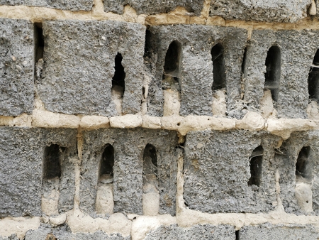 The texture of a fragment of a light gray wall with dark holes, in a natural environment