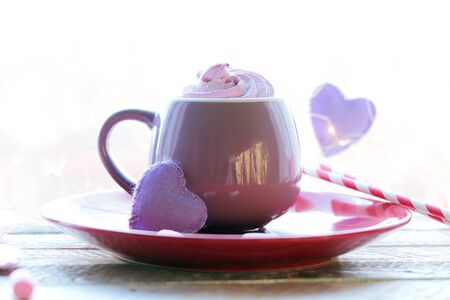Cup of coffee with meringues and marshmallows, hearts, illumination on a wooden windowsill