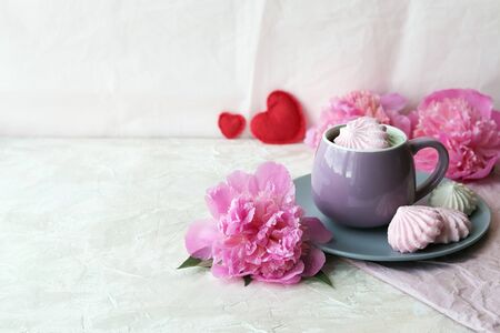 Cup of coffee with meringues, pink peony flowers, hearts on a light background, romantic breakfast conceptの写真素材