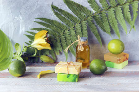 Soap, limes and bottles with aromatic oil, lily flower on a wooden table, natural cosmetics for home body careの写真素材