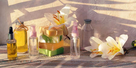 Soap, antiseptic spray and bottles with aromatic oil, white lily flower on a wooden background,...