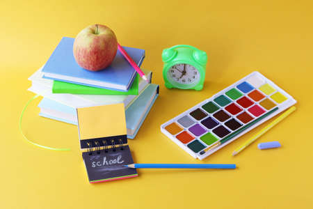 Back to school, stationery, alarm clock, stack of books, apple on bright background, preparation of accessories for learning, at homeの写真素材