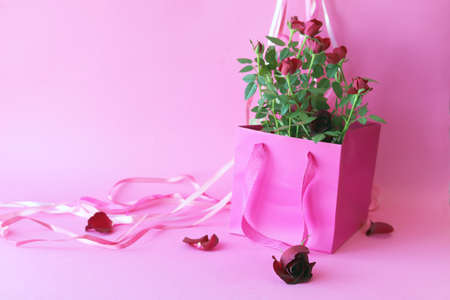 Fresh roses are packed in a pink bag on a light background for a romantic giftの写真素材