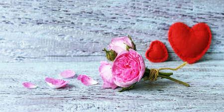 A small bunch of fresh roses, a pair of red felt hearts on a wooden surface, background for romantic...