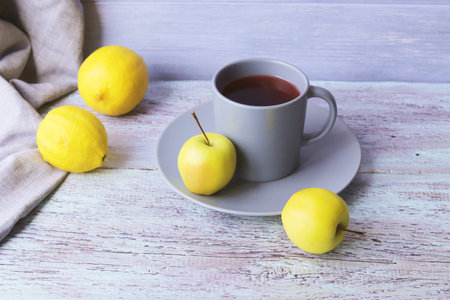 Hot tea in a large cup, lemons and apples on a wooden table, yellow and gray color, vitamin drink concept, home comfortの写真素材