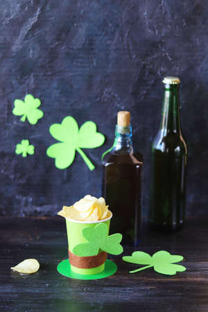 Beer, chips in a paper glass in the shape of St. Patrick's hat, shamrock on a dark background,...